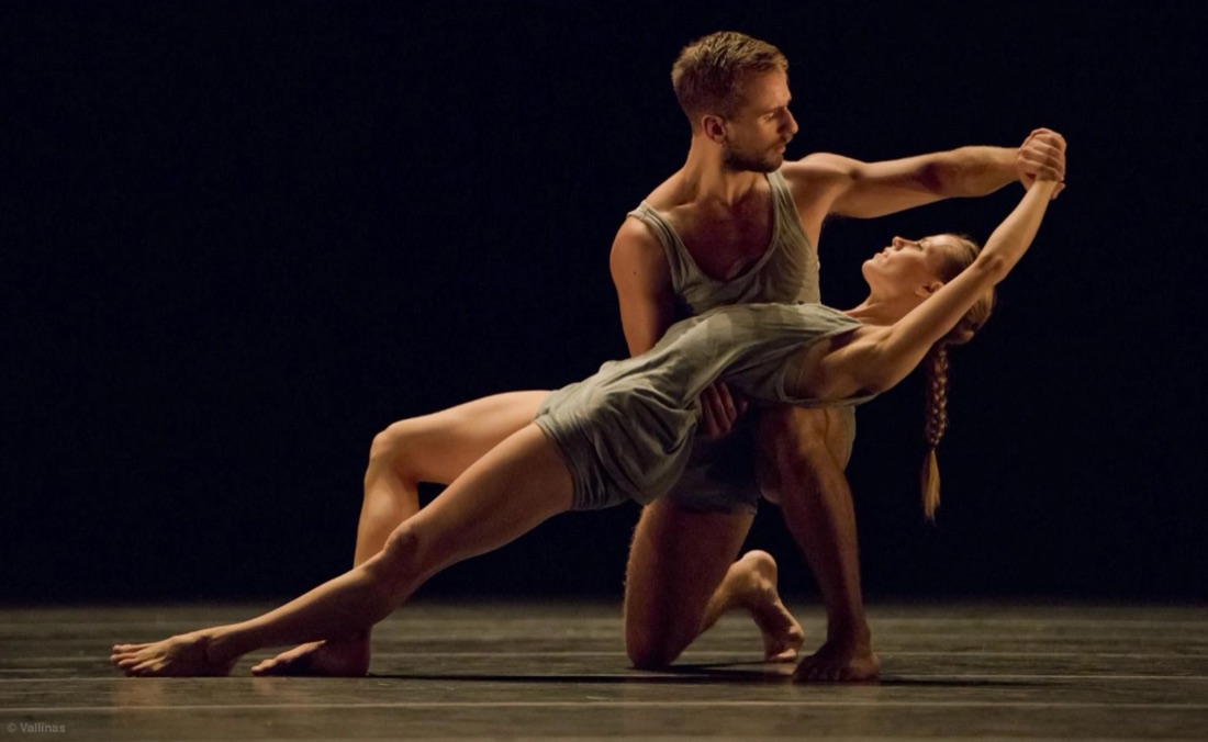 Daan bailando en un escenario oscuro, sosteniendo a una compañera en una pose de danza contemporánea.